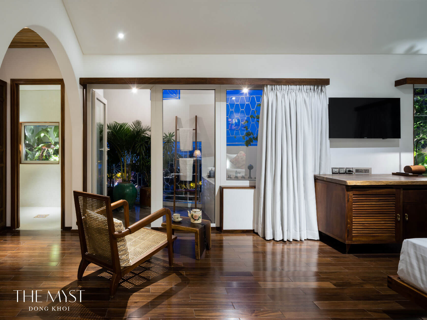 A room at The Myst Dong Khoi with sliding glass doors open onto a planted balcony