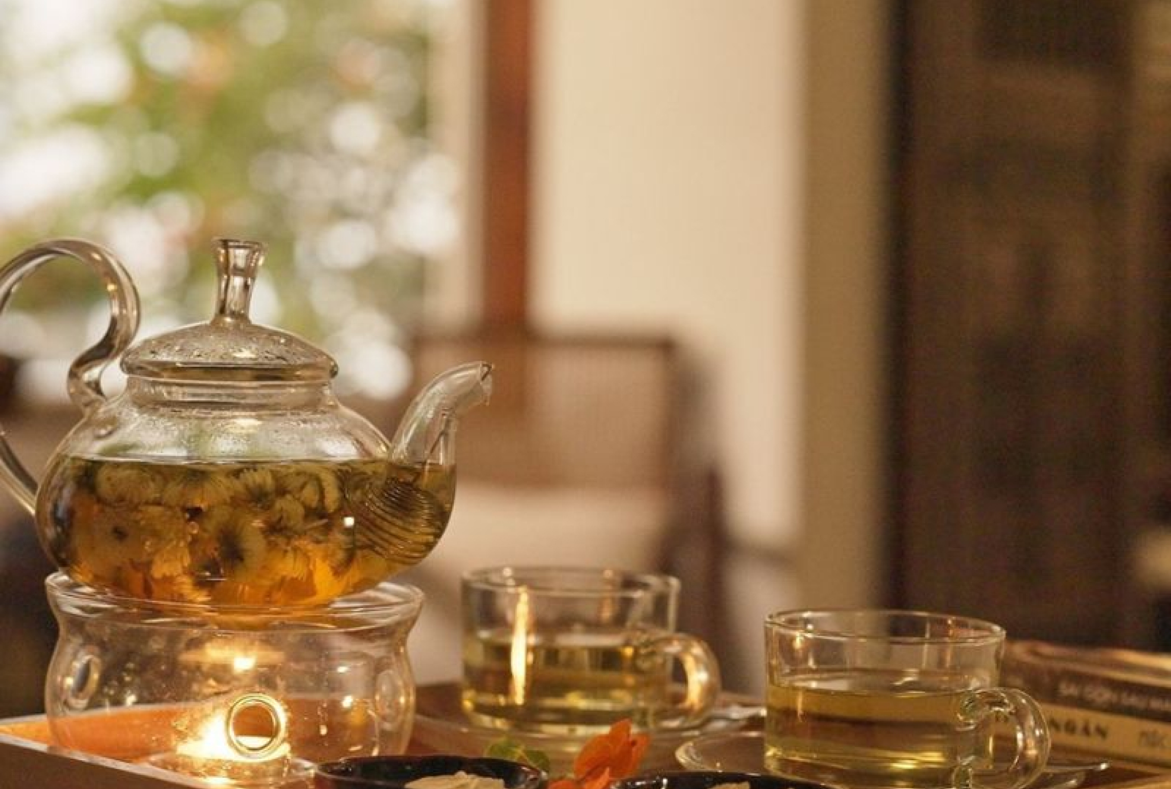 A glass teapot of flowering tea and small glasses in calm afternoon light