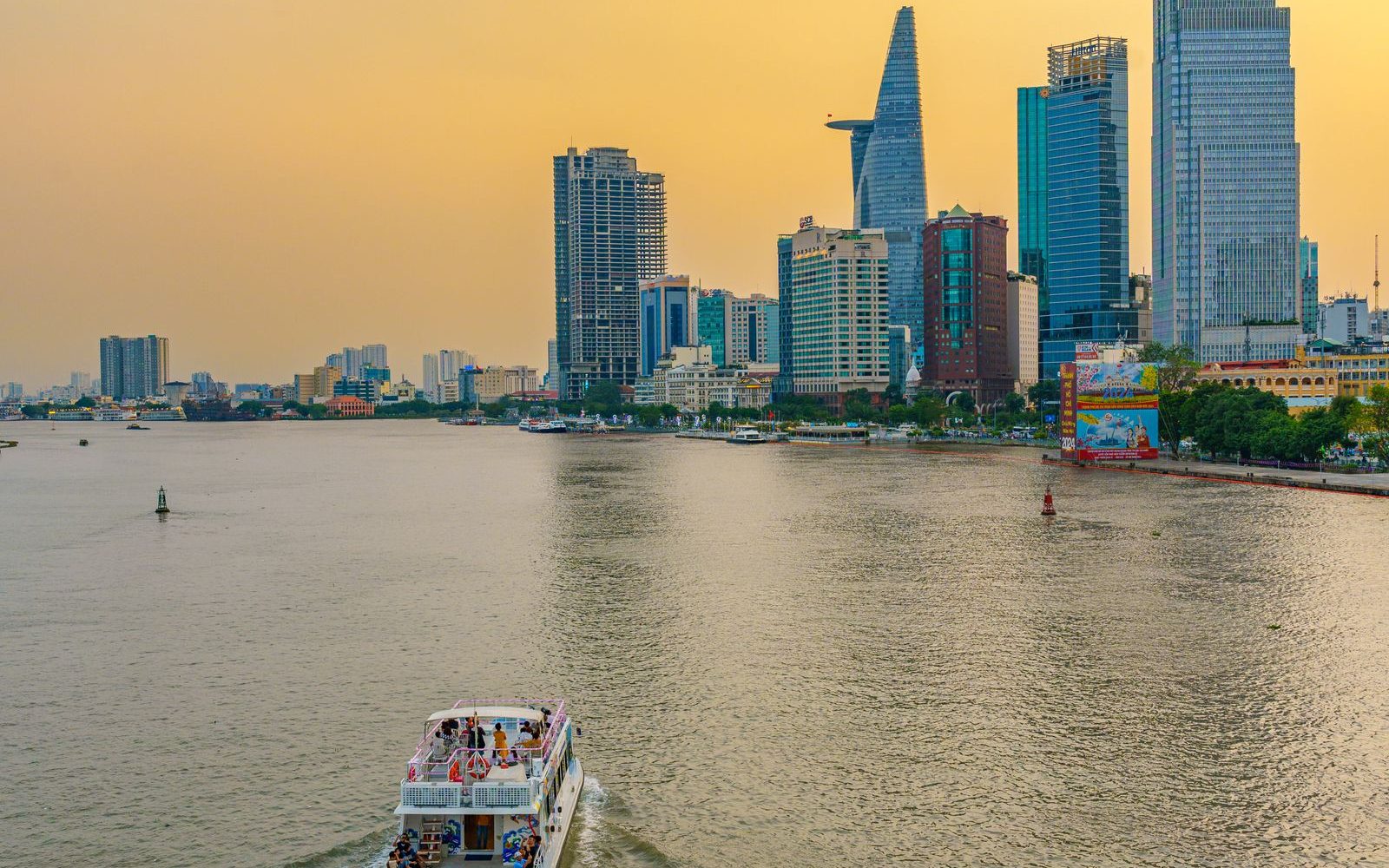 A boat on the Saigon River at golden hour with the city skyline, seen from a riverside terrace in Thao Dien